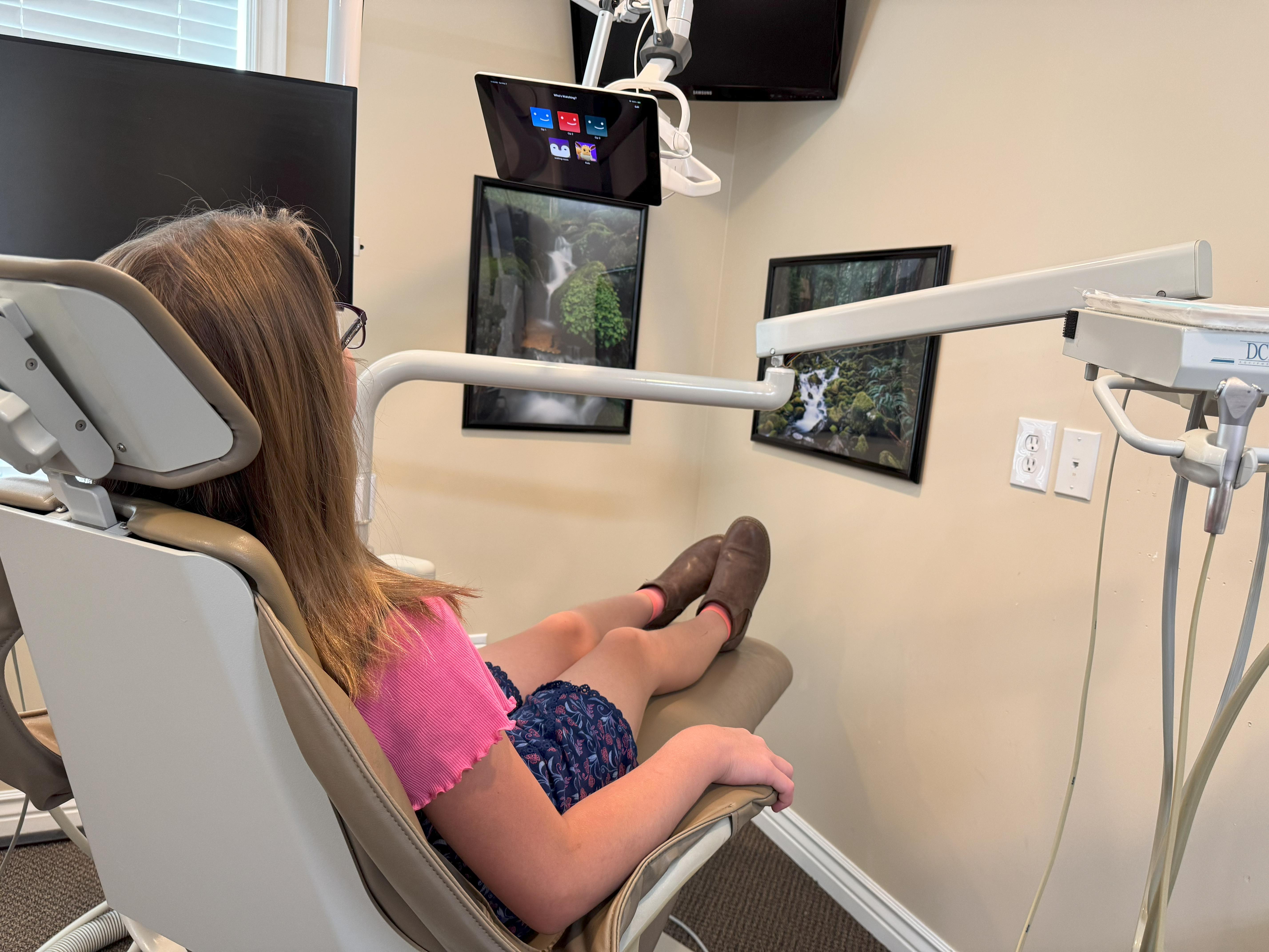 A girl sitting in the dentist chair watching tv