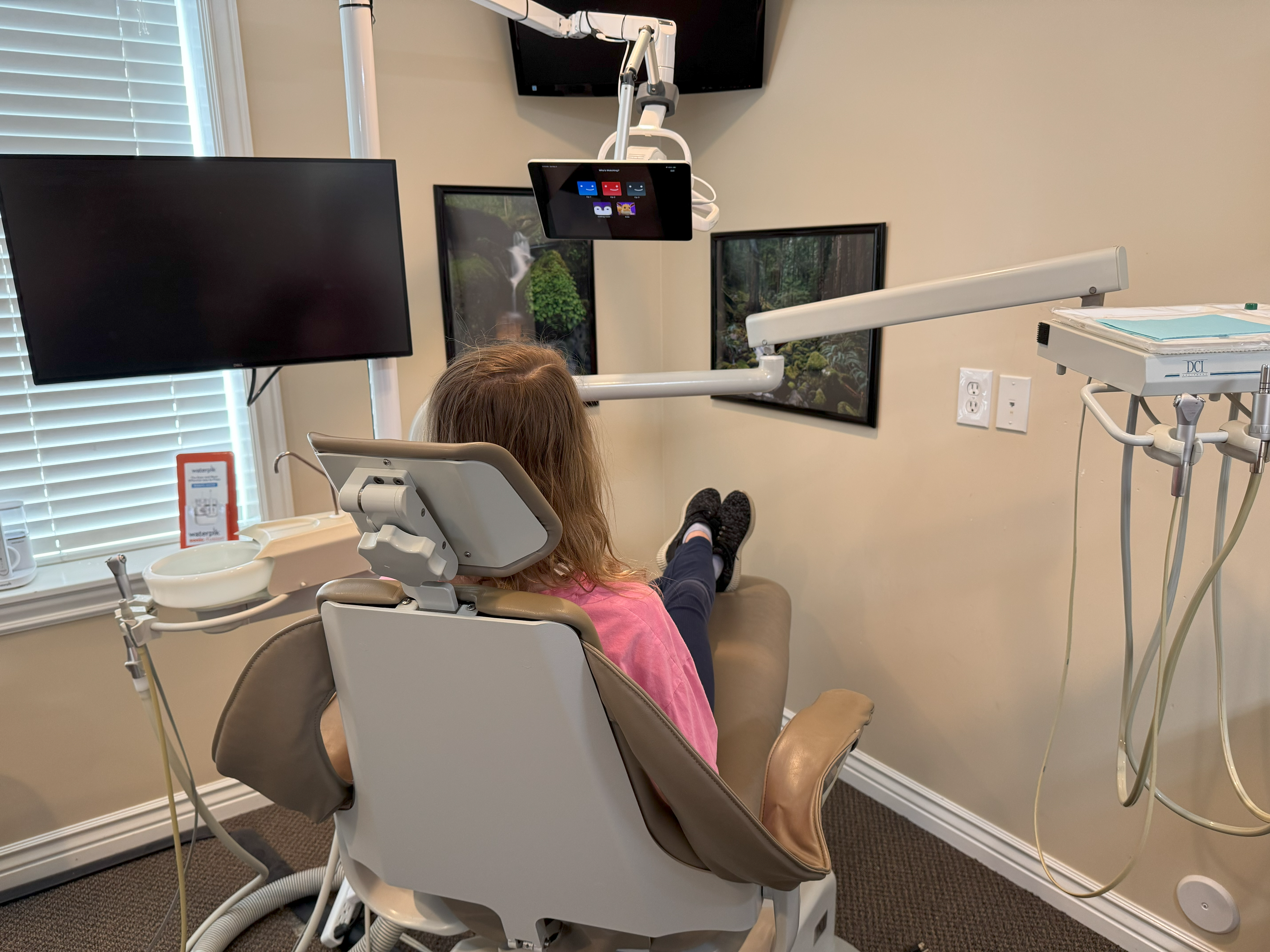 A girl sitting in the dentist chair watching tv